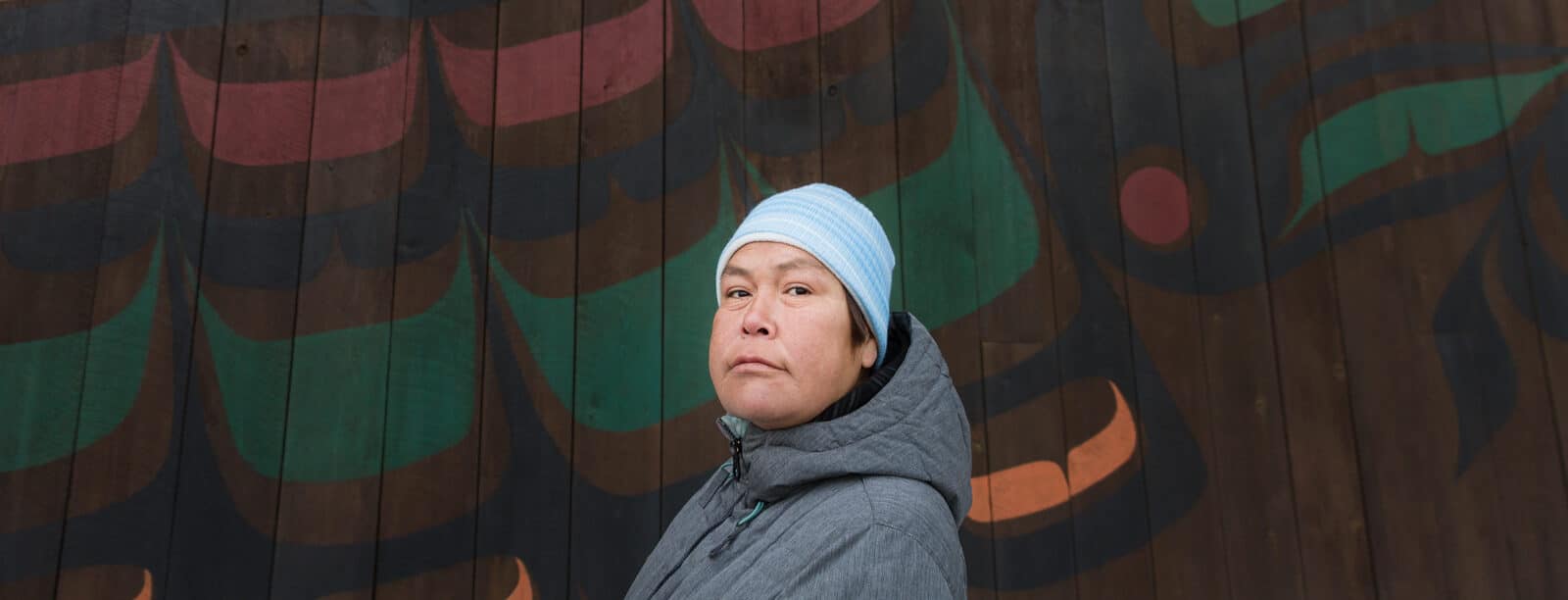 man wearing a touque standing in front of indigenous art